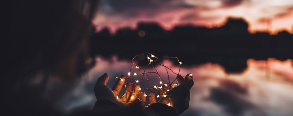 Person holding fairy lights in their hands in front of dramatic sunset