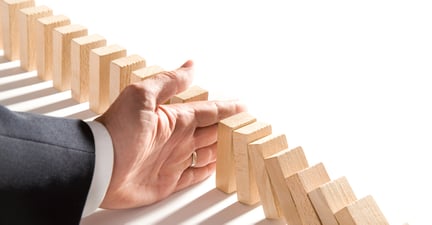 Hand of a businessman stopping the chain of falling dominoes